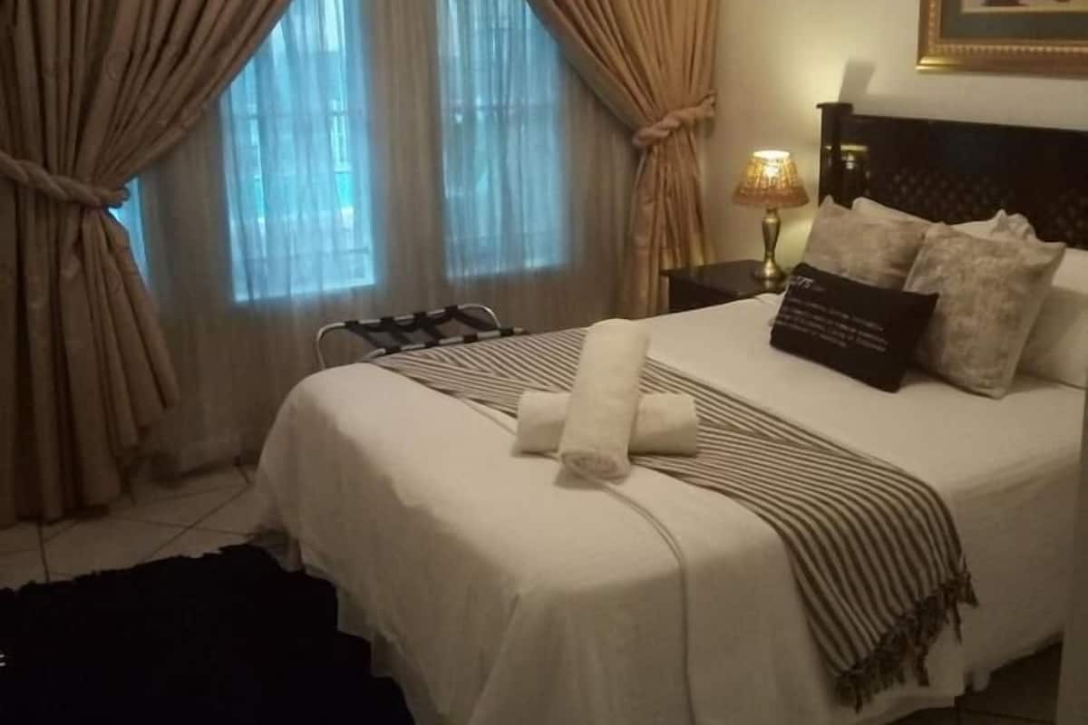 Cama bem arrumada com manta listrada e toalhas dobradas, cabeceira com travesseiro, mesa de cabeceira com abajur e quadro na parede.