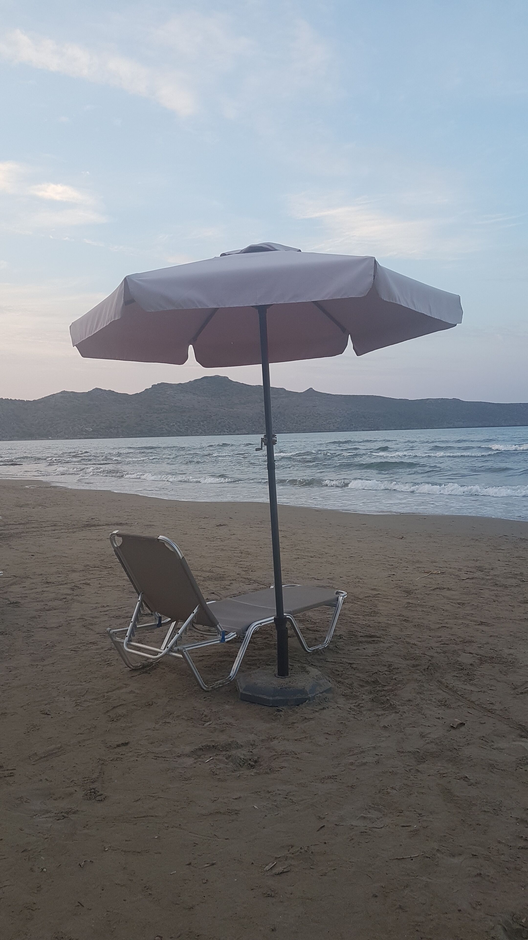 A beach with a single beach chair and an umbrella.