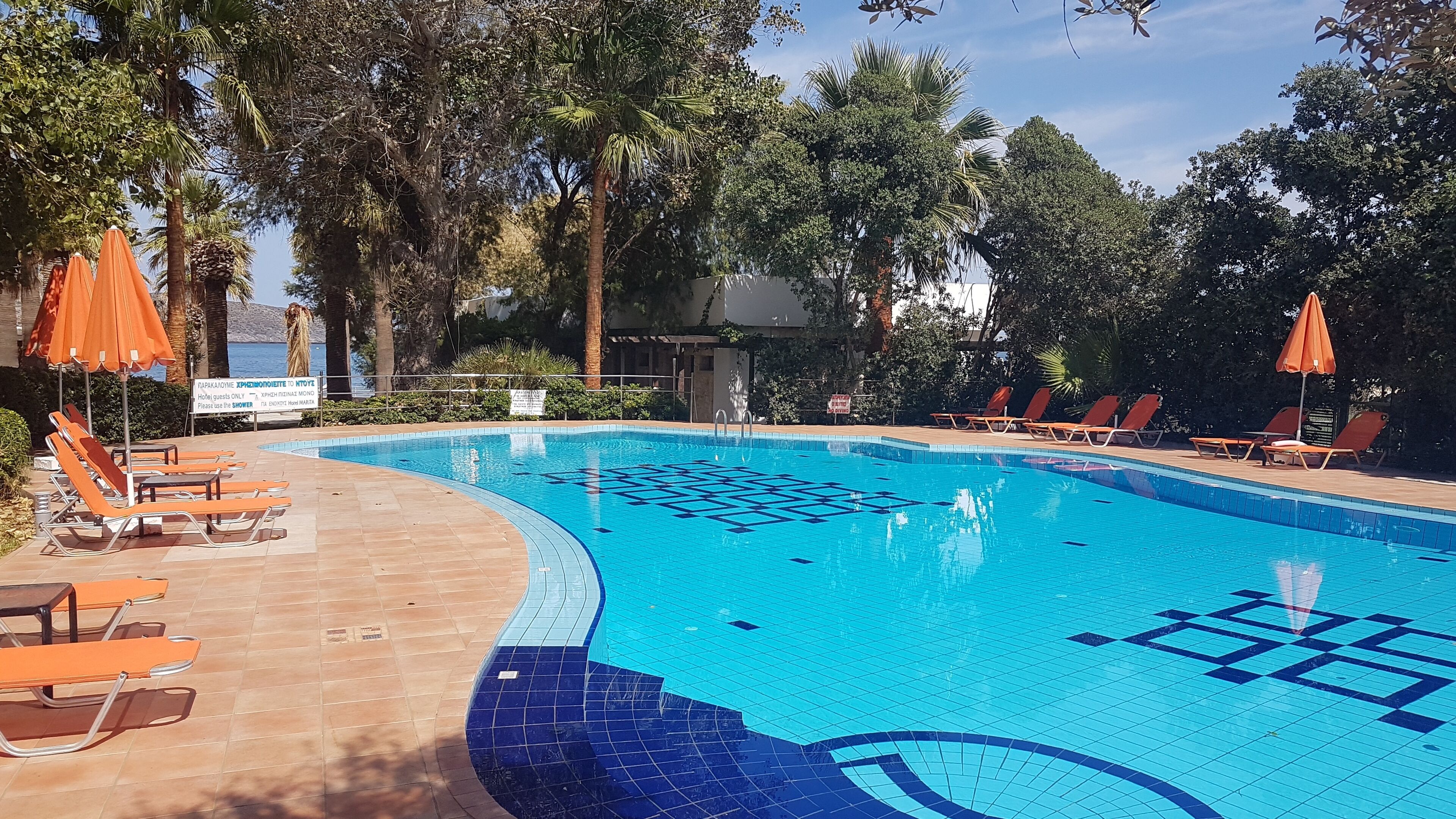 Una piscina amb motius de rajoles, envoltada de gandules i para-sols taronja.