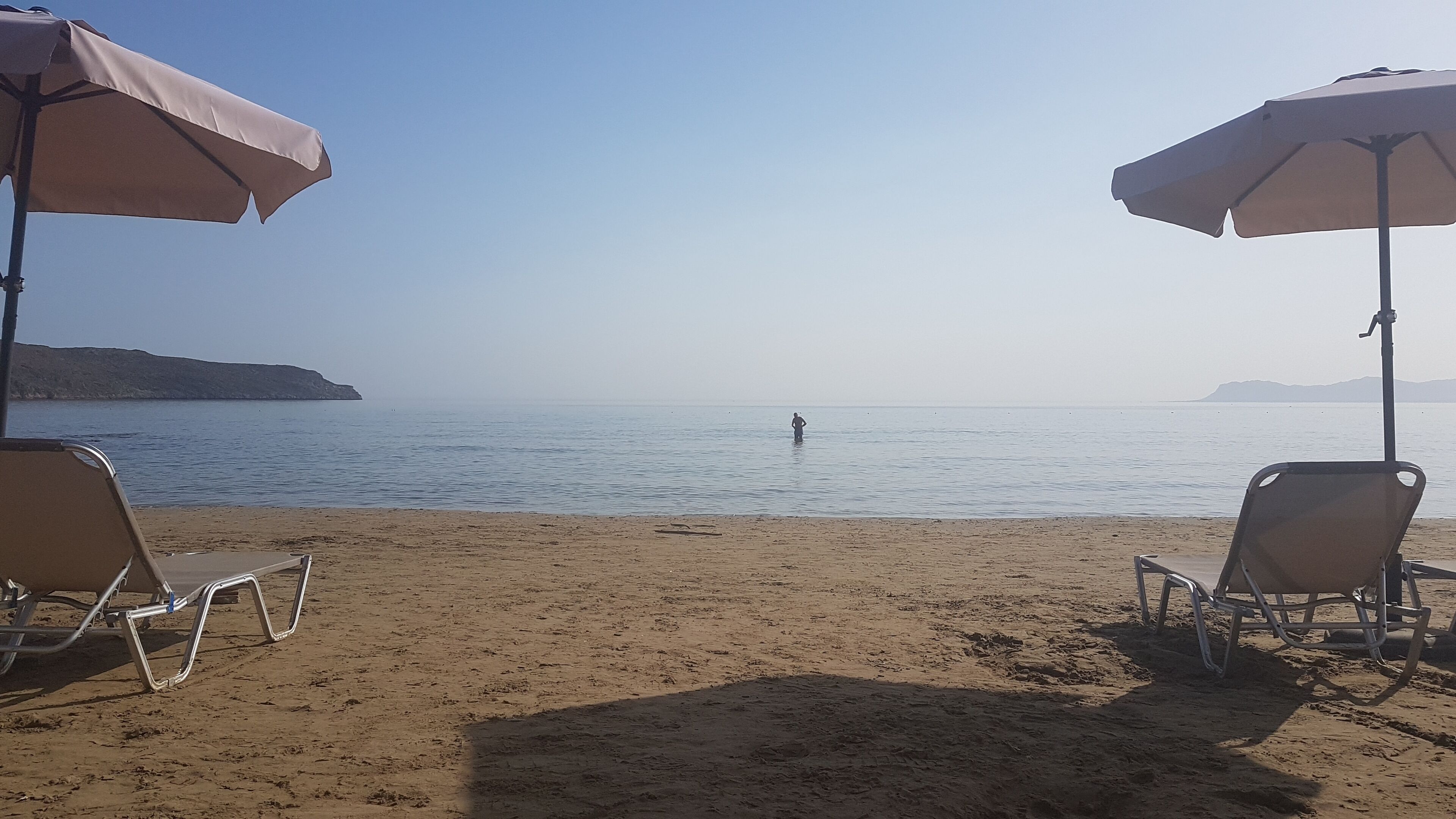 A beach with two sun umbrellas and beach chairs.
