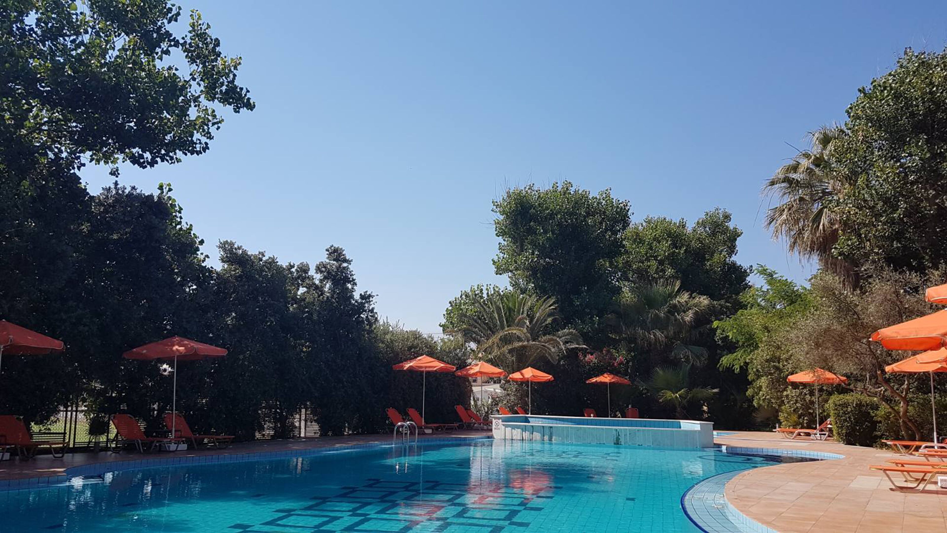 A swimming pool with multiple lanes, surrounded by red umbrellas and lounge chairs.