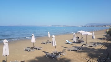 A beach with sun loungers and umbrellas, a clear sky, and a calm sea.