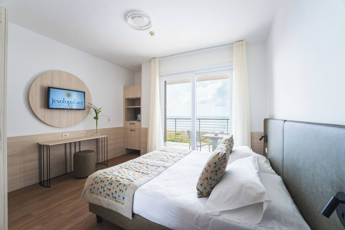 A hotel room with a bed, a desk, a chair, a TV, and a balcony with a view.