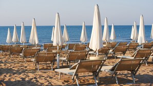 Ein Strand mit Reihen von Liegestühlen und weißen Sonnenschirmen, der zum Meer hin ausgerichtet ist.