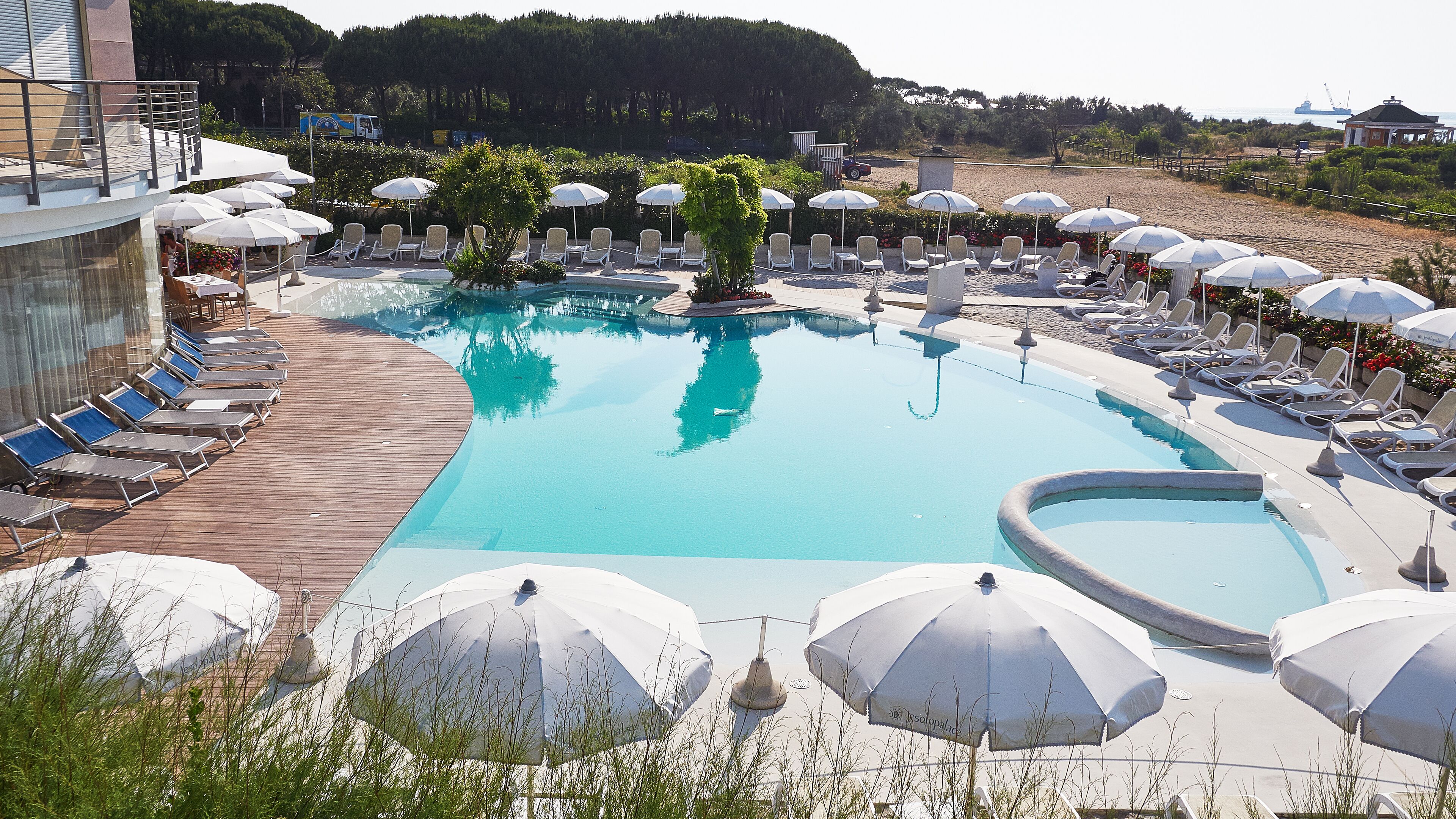 A pool area with sun loungers and umbrellas, surrounded by a wooden deck and a landscaped garden.