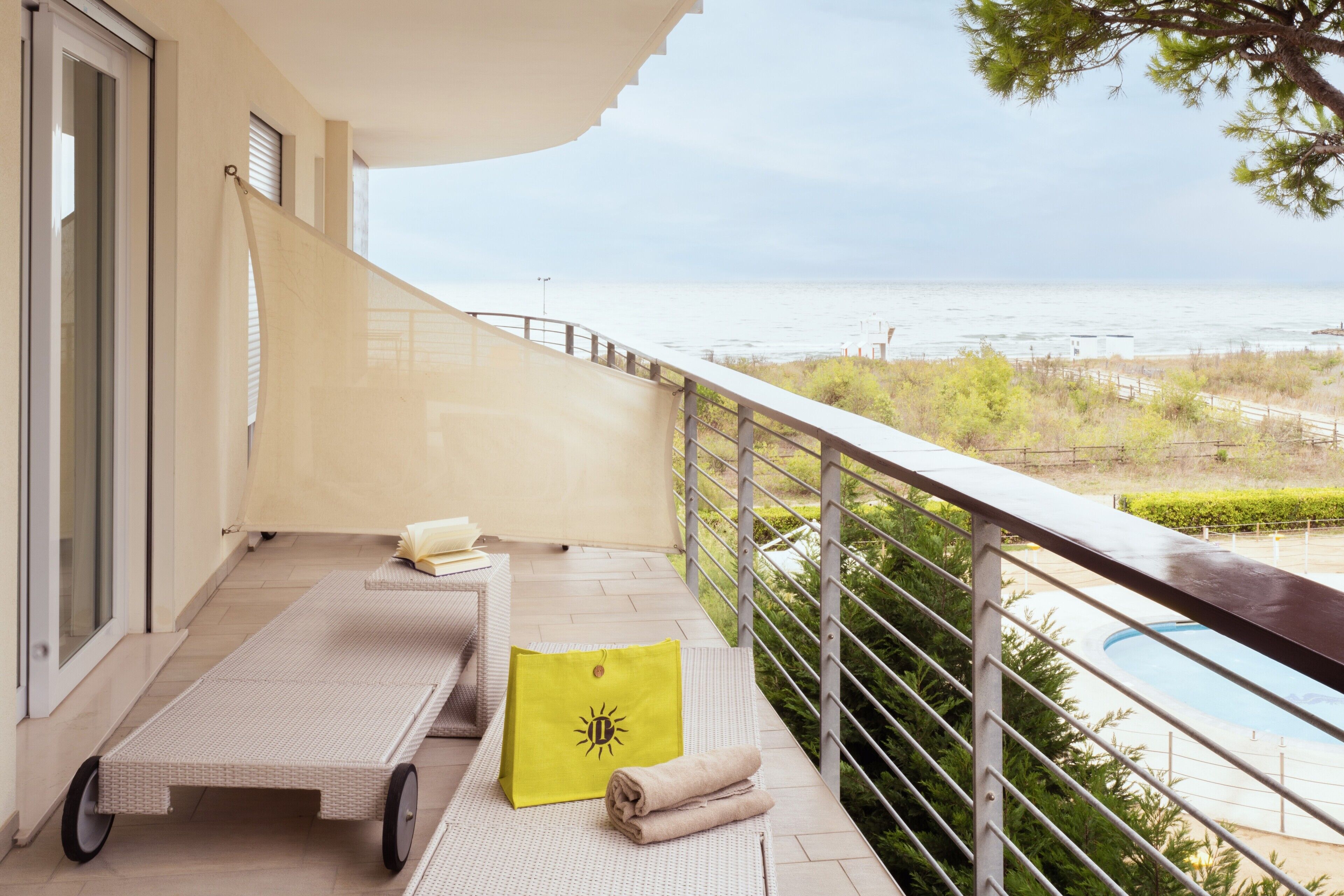 Un balcón con vista al mar, una piscina y una toalla de playa.