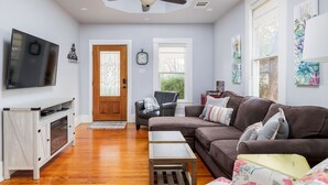 A living room with a brown sofa, a TV mounted on the wall, and a ceiling fan.
