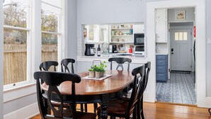 A dining area with a wooden table and chairs, a chandelier, and a view of a wooden fence outside.