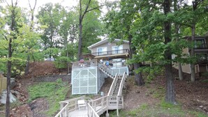 A wooden bridge leading to a house with a balcony, surrounded by trees and a small stream. - Great Location!  Heart of Horseshoe Bend-2MM in Lake of the Ozarks. (Lake Ozark)
