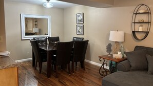 A dining area with a table and chairs, a mirror, framed pictures, a lamp, and a shelf with decorative items. - Great Location!  Heart of Horseshoe Bend-2MM in Lake of the Ozarks. (Lake Ozark)