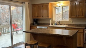 A kitchen with wooden cabinets, a large island with stools, a coffee maker, and a view of a deck with chairs. - Great Location!  Heart of Horseshoe Bend-2MM in Lake of the Ozarks. (Lake Ozark)
