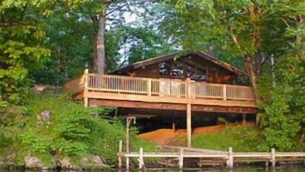 Une cabane en bois dotée d’une terrasse, entourée d’une végétation luxuriante et bordée par un plan d’eau.