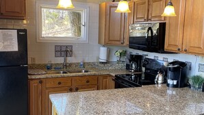 Une cuisine avec des meubles en bois, des plans de travail en granit, un réfrigérateur noir, un four à micro-ondes, une cuisinière et deux tabourets de bar.