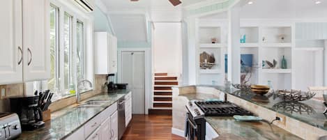 A spacious kitchen with white cabinetry, a central island, and a staircase leading to another level.