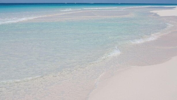 Een strand met helder turquoise water en wit zand.