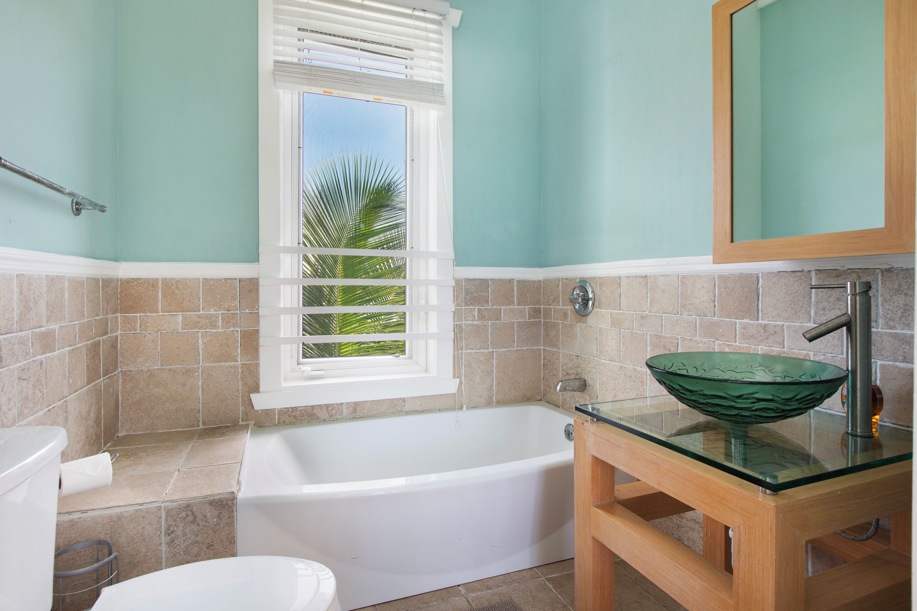 Une salle de bain avec une baignoire, un lavabo en verre et une fenêtre avec des stores.