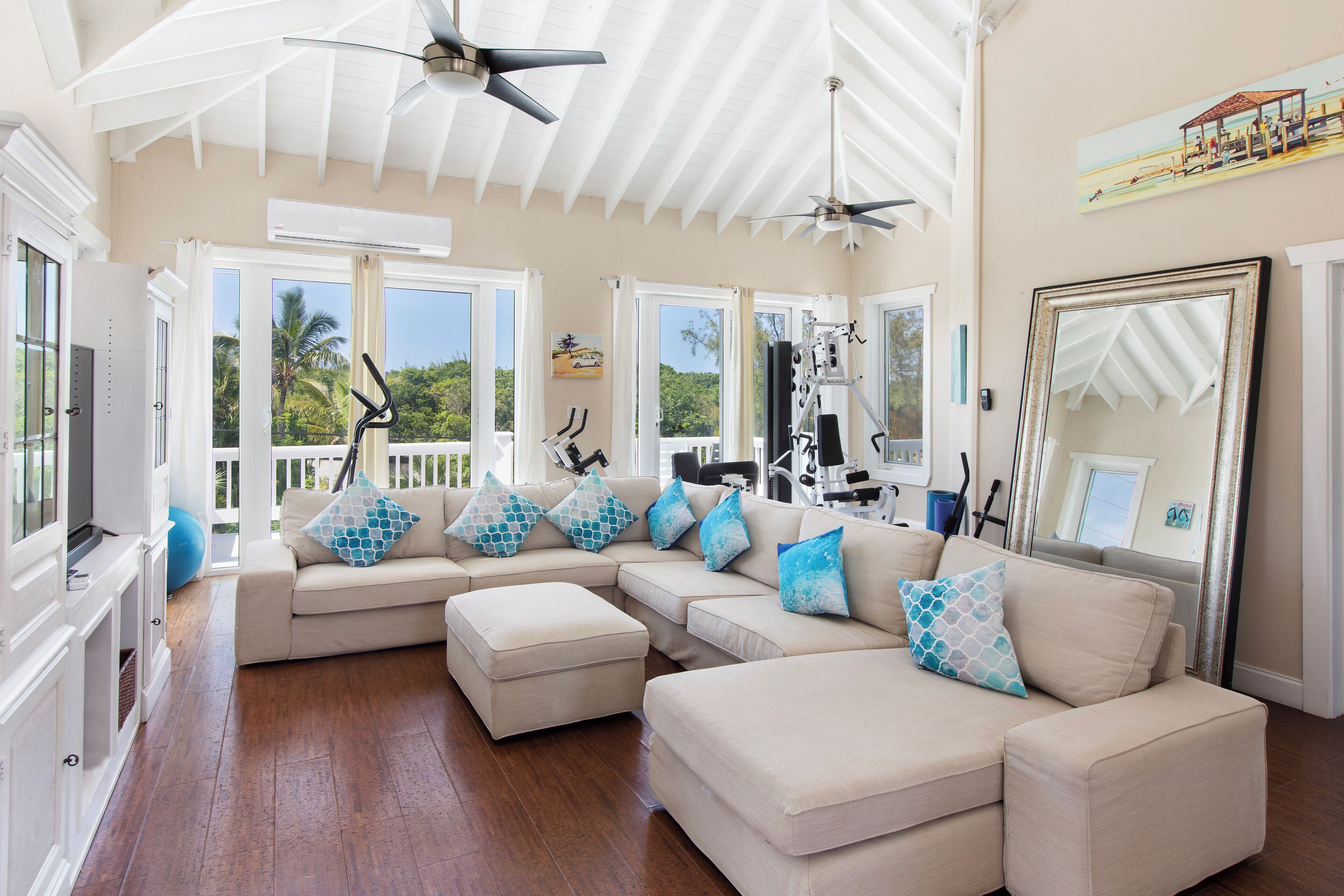 A spacious living room with a large sectional sofa, exercise equipment, and a ceiling fan.