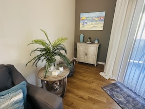 A living room with a sofa, a small round table with a plant, a cabinet with decorative items, and a painting on the wall.