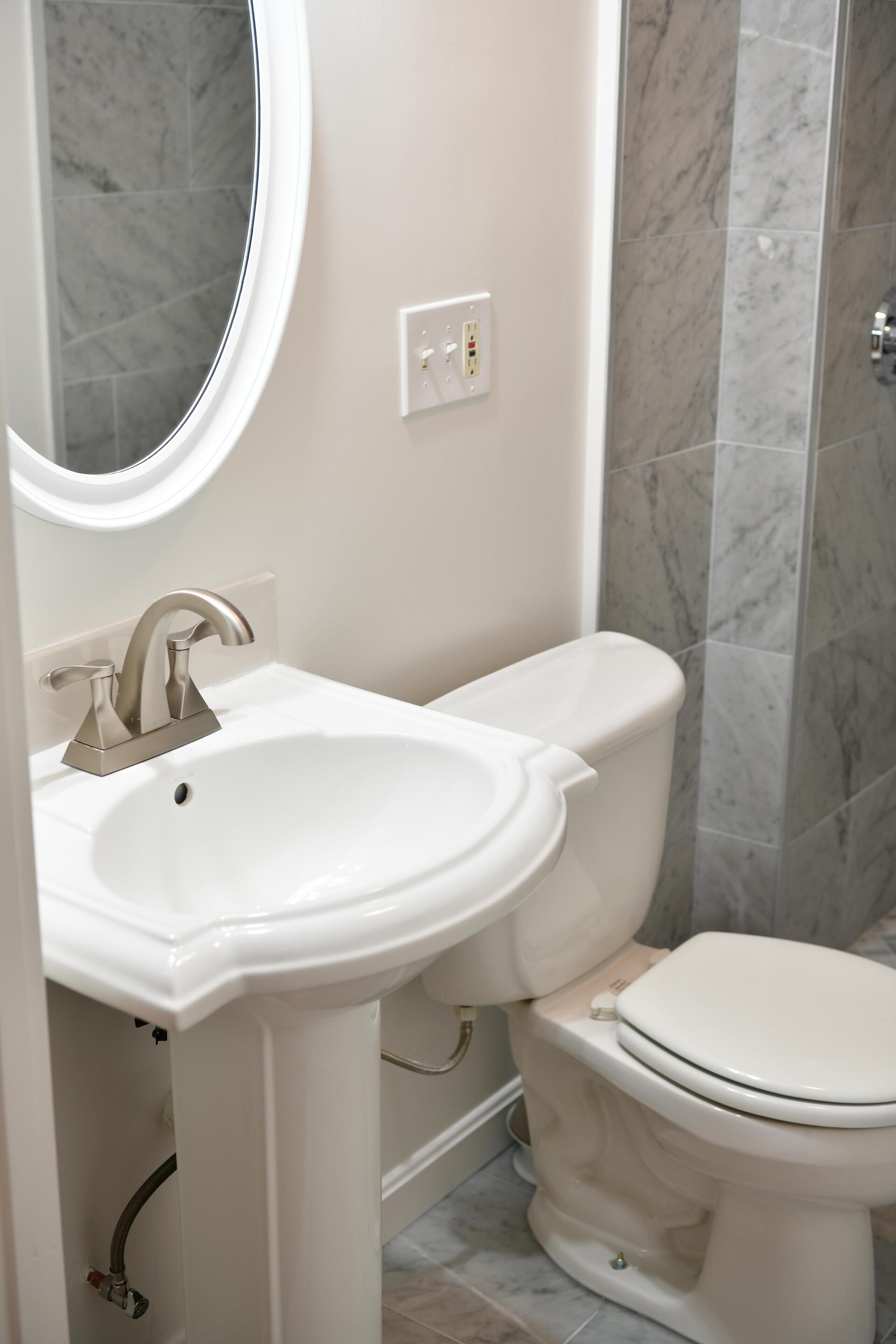 A bathroom with a white sink, a toilet, and a marble-tiled shower area.