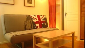 A room with a sofa against a wall, a wooden table in the center, and a door with a handle. - RENT CHARMING STUDIO (Cauterets)