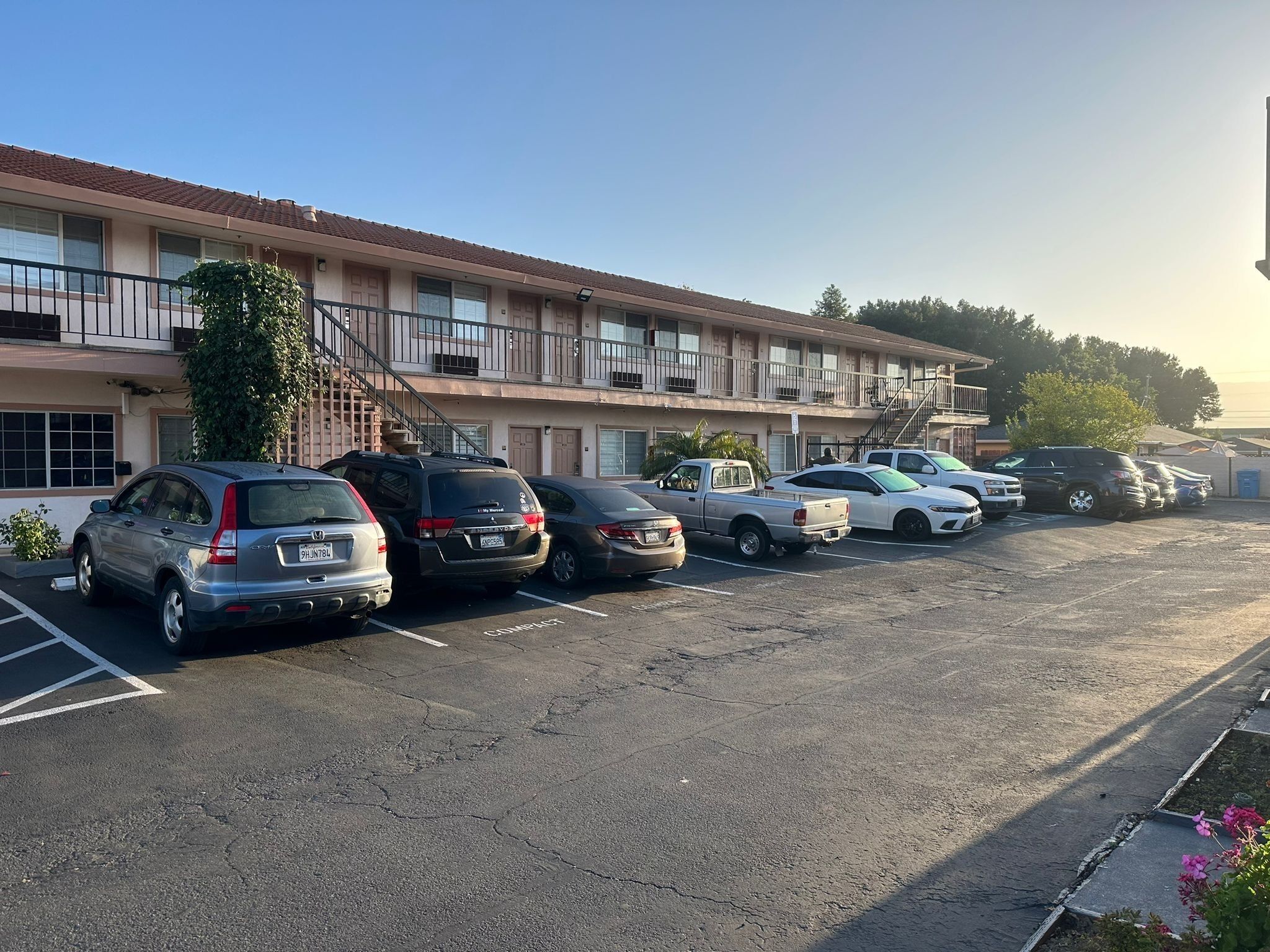 A parking lot with several cars parked in front of a motel with multiple balconies and a staircase leading to the entrance.