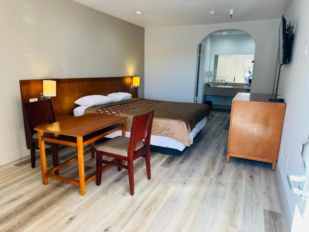 A hotel room with a bed, a wooden desk, a chair, a small cabinet, and a bathroom visible through an archway.