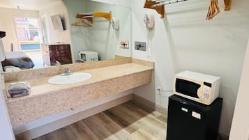 A bathroom with a sink, mirror, towel rack, and a microwave on a small cabinet.