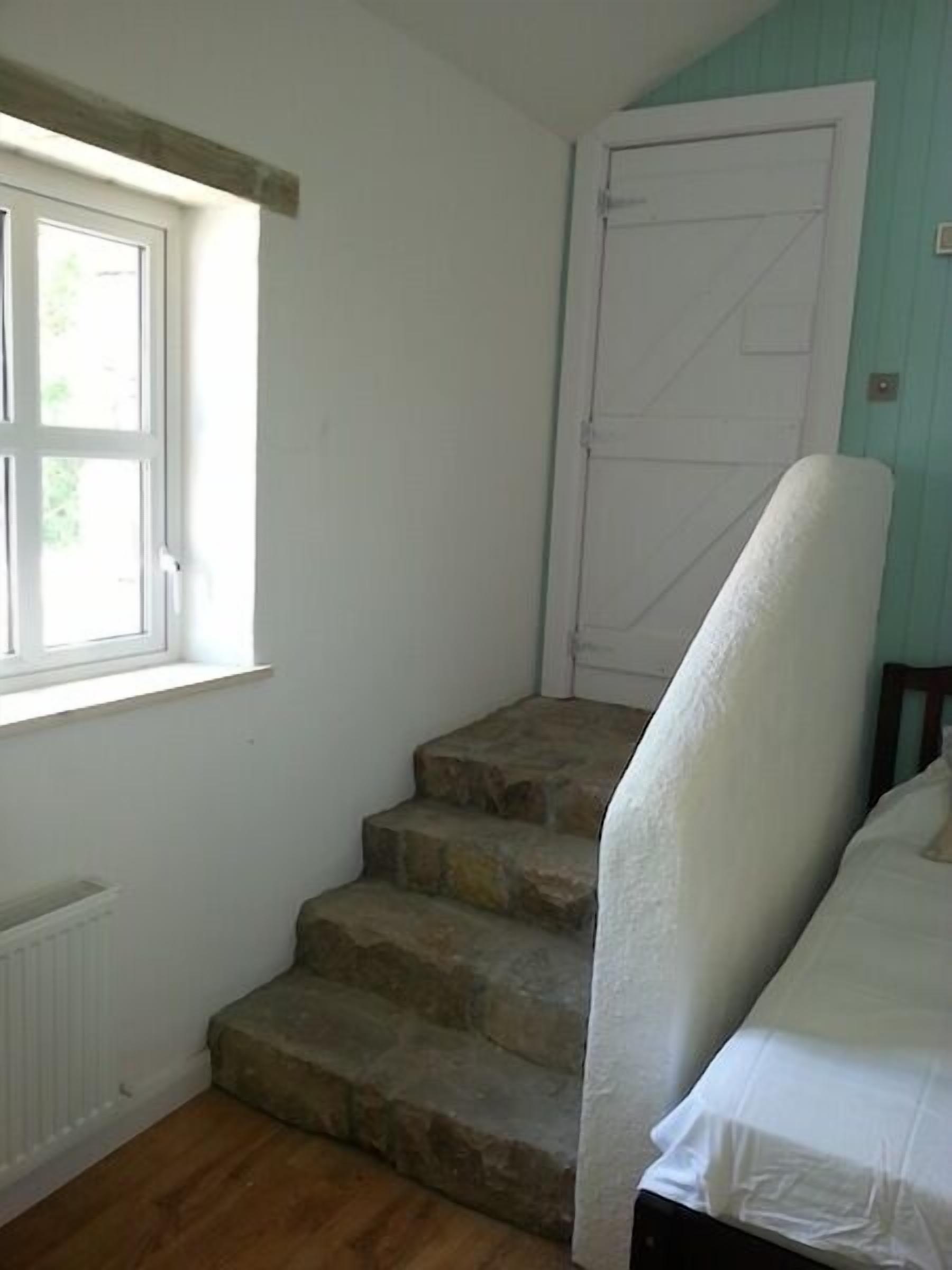 A room with a stone staircase, a white door, and a window with a view of greenery outside.