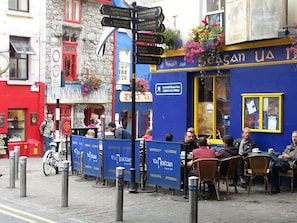 A street scene with a blue building, a signpost with directions, and people sitting outside. - Connemara Stone Barn on Wild Atlantic Way, walk to beach, near Aran Island Ferry (Inverin)