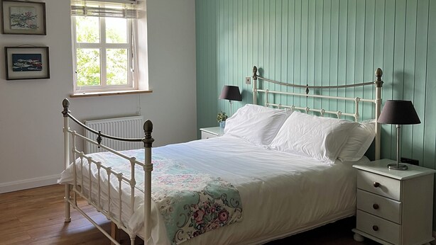 A bedroom with a bed, bedside tables, a window, and a ceiling fan. - Connemara Stone Barn on Wild Atlantic Way, walk to beach, near Aran Island Ferry (Inverin)