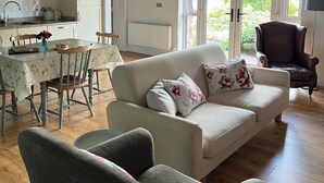 A cozy living room with a sofa, chairs, a dining table, and a kitchen area with stone walls and wooden beams. - Connemara Stone Barn on Wild Atlantic Way, walk to beach, near Aran Island Ferry (Inverin)