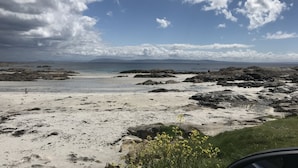 A beach with rocky terrain, a sandy area, and a distant view of mountains under a partly cloudy sky. - Connemara Stone Barn on Wild Atlantic Way, walk to beach, near Aran Island Ferry (Inverin)