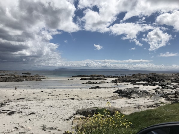 A beach with rocky terrain, a sandy area, and a distant view of mountains under a partly cloudy sky. - Connemara Stone Barn on Wild Atlantic Way, walk to beach, near Aran Island Ferry (Inverin)