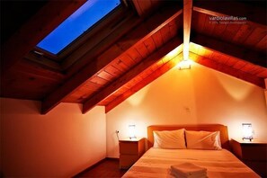 A cozy attic bedroom with a skylight, wooden beams, and a neatly made bed.