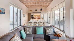 A spacious living area with a gray sofa, teal cushions, and a wooden coffee table with a tray of tea. A dining area with a white table and chairs is visible in the background. - Modern and Stylish Villa with Private Pool & Spectacular Views to the Aegean Sea (Chania)