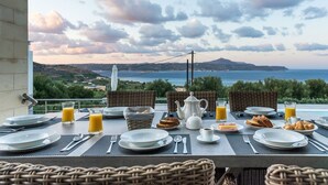 A breakfast table set with plates, cutlery, and breakfast items, overlooking a scenic coastal view. - Modern and Stylish Villa with Private Pool & Spectacular Views to the Aegean Sea (Chania)