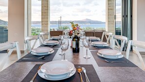 A dining table set for six with a bottle of wine, glasses, and plates, overlooking a scenic view. - Modern and Stylish Villa with Private Pool & Spectacular Views to the Aegean Sea (Chania)