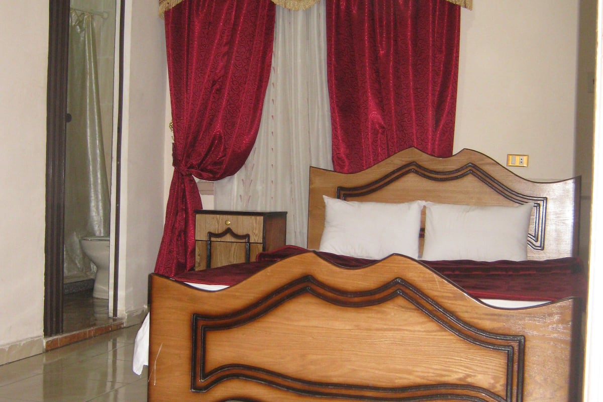 Une chambre à coucher avec un lit en bois, des rideaux rouges, un oreiller blanc et un miroir.