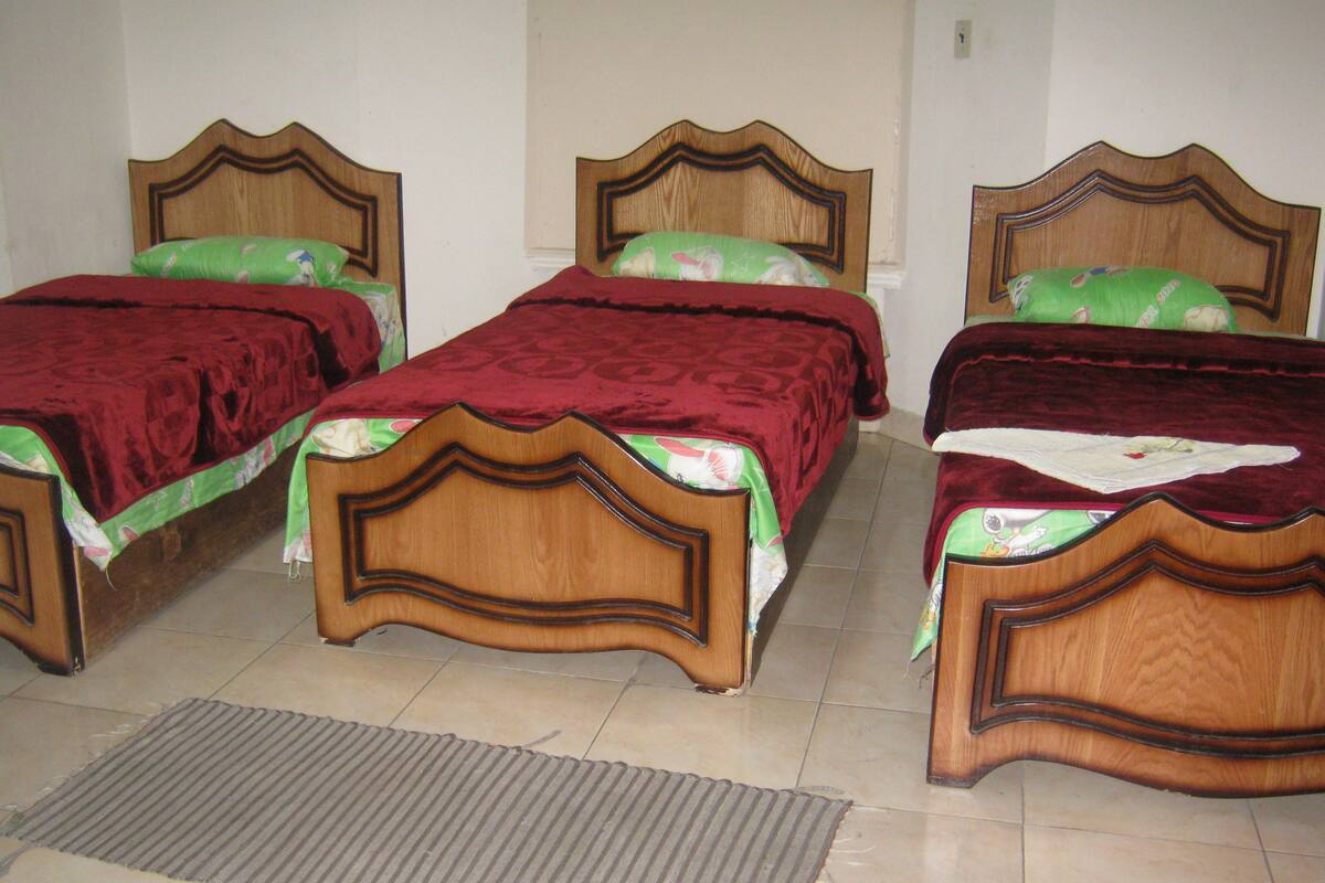 Une pièce comprenant trois lits en bois, chacun doté d’une tête de lit au design distinct, disposés en rangée.