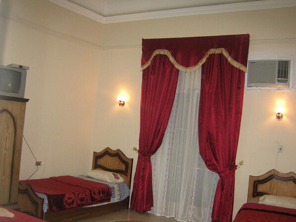 Une chambre à coucher avec deux lits en bois, des rideaux rouges et des lampes fixées au mur.