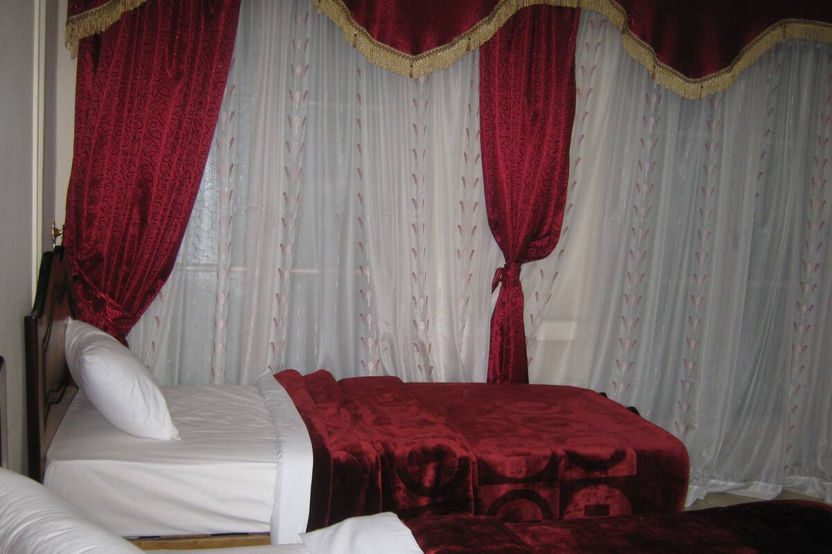Une chambre avec deux lits, l’un recouvert d’une couvre-lit rouge et l’autre de draps blancs.