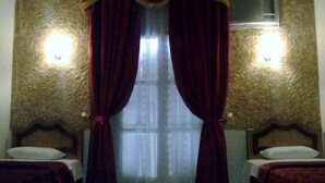Une chambre avec deux lits, une fenêtre avec des rideaux légers et un mur à motifs.