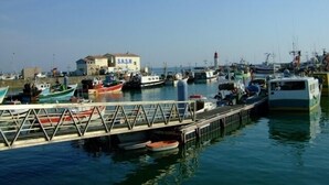 Un puerto deportivo con varios barcos amarrados, un edificio con la leyenda 'S.N.S.M.' y un cielo despejado.