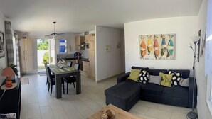 Una sala moderna con un sofá oscuro, una mesa de comedor y una cocina al fondo.
