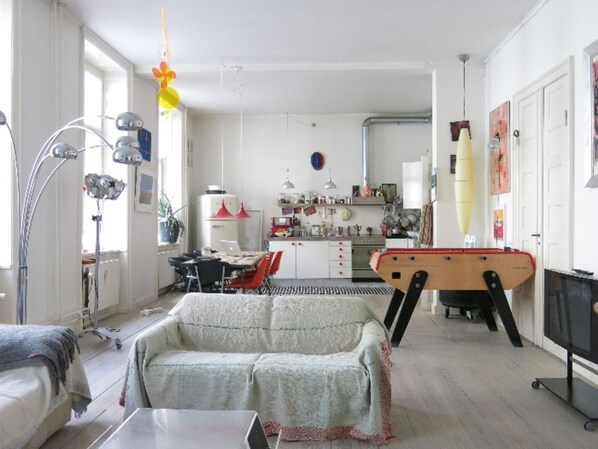 A spacious living room with a sofa, a dining table, and a kitchen in the background.