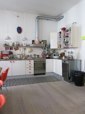 A compact kitchen with white cabinets, a built-in oven, and a sink. There are hanging pots and pans, and a coffee machine on the counter.