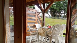 A covered patio area with a table and chairs, a wooden fence, and a grassy yard visible through the window. - Lovely, quiet 4-star apartment for two - close to village and lake - Wi-Fi (Titisee-Neustadt)