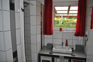 A modern bathroom with a shower, a sink, and a window with red curtains.
