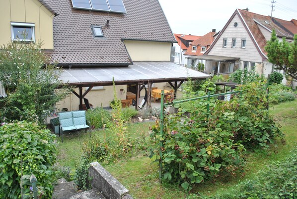 A residential house with a covered patio, a garden with various plants, and a bench.