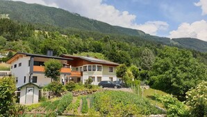 A two-story house with a balcony, surrounded by lush greenery and mountains. - Large 105m² apartment with terrace for 4 to 6 persons & beautiful south view! (Flattach)